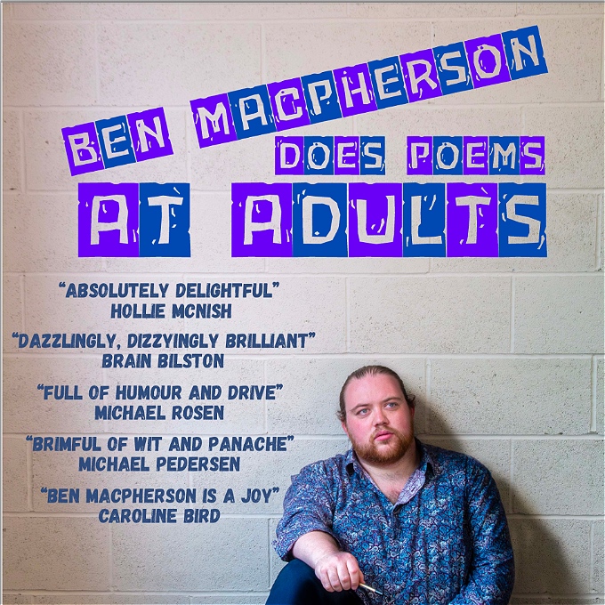 A man with brown hair and a large red beard sits in front of a wall, holding a pen