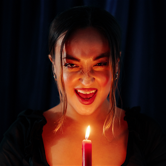 Female comedian on dark background laughing maniacally, holding a candle