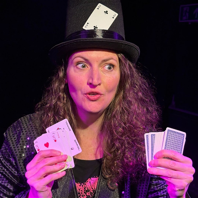 Kath is wearing a magician's hat and is holding playing cards