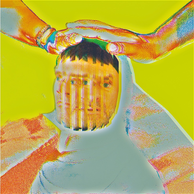 A male comedian in psychedelic colours, being patted on the head by the hands, wrapped in a cloth, with a distorted face that suggests an identity crisis,