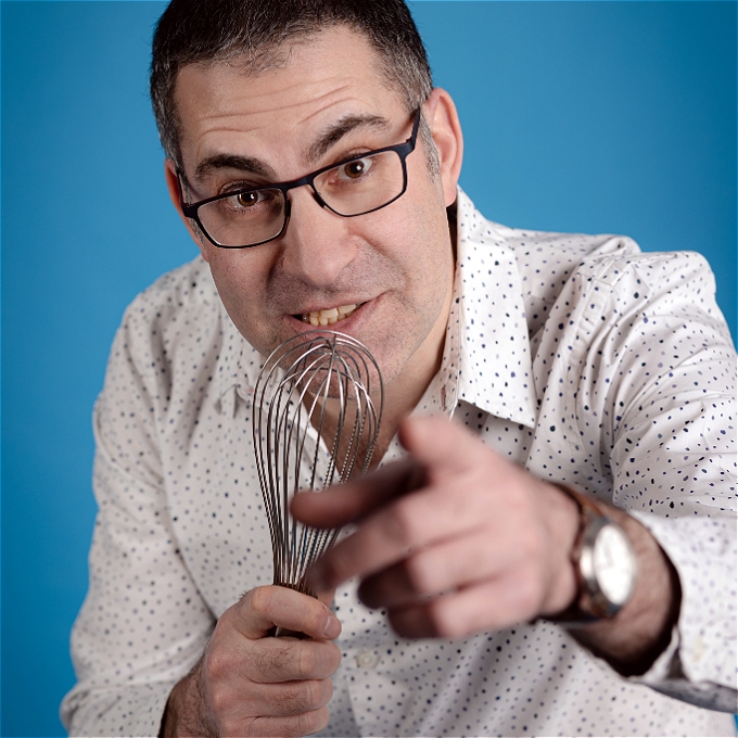 Male stand-up wearing glasses holding whisk