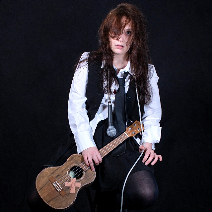 Femme comedian looking tired holding a broken ukelele