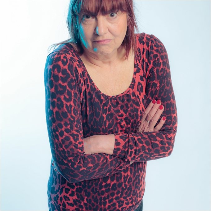 Female comedian with folded arms in front of a blue background.