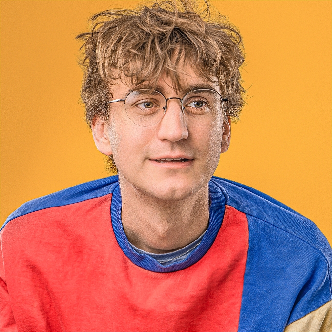 male comedian with glasses looking into the middle distance