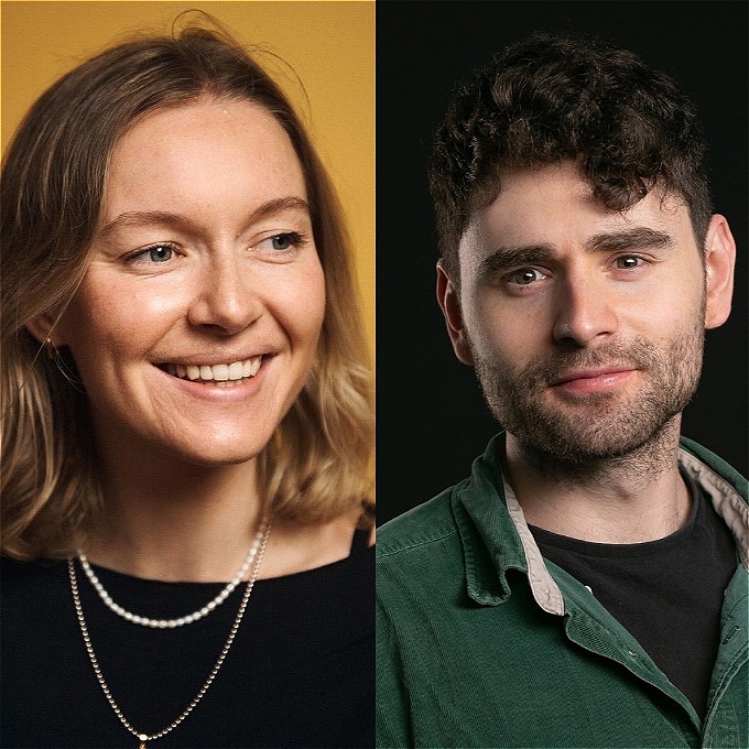 Two smiling comedians in front of a blank background