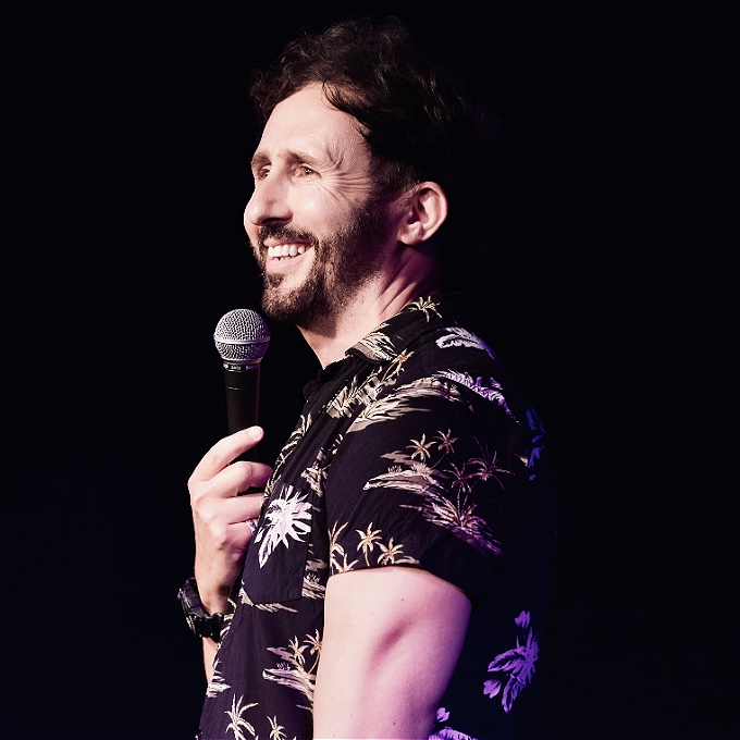 Nathan Cassidy, comedian, smiling and holding a mic