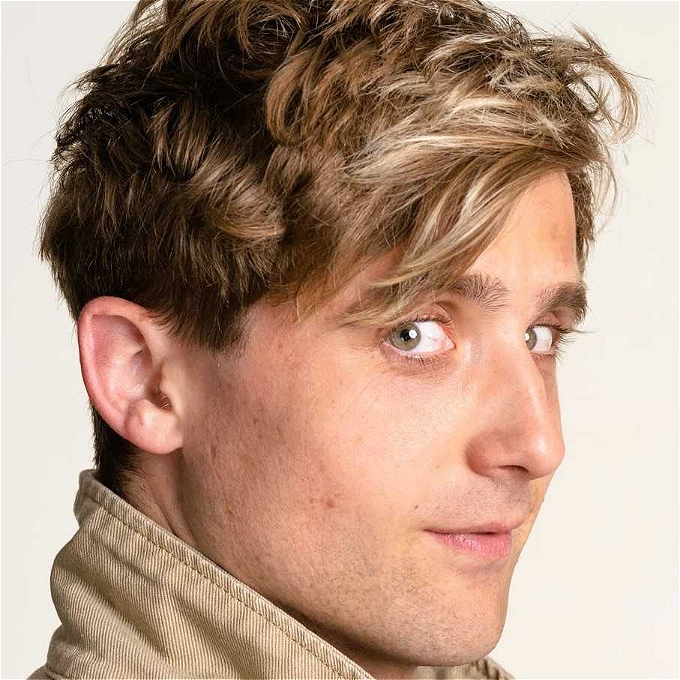 Male comedian with brown hair smiling at the camera