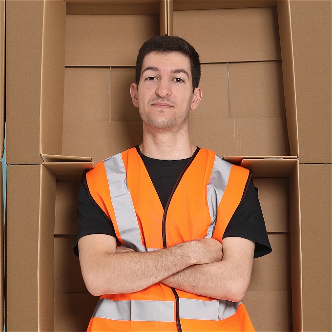 Male Comedian wearing high viz with his arms folded and a background of boxes