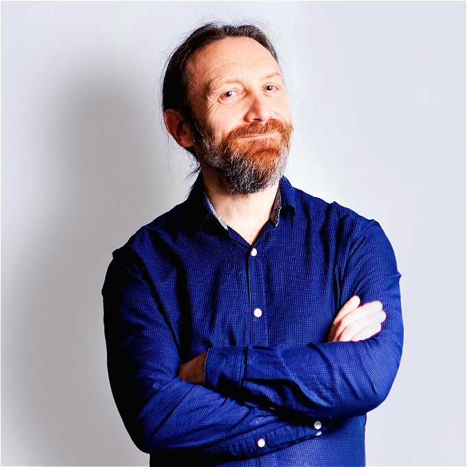 Smiling man with beard in a blue shirt and with arms folded