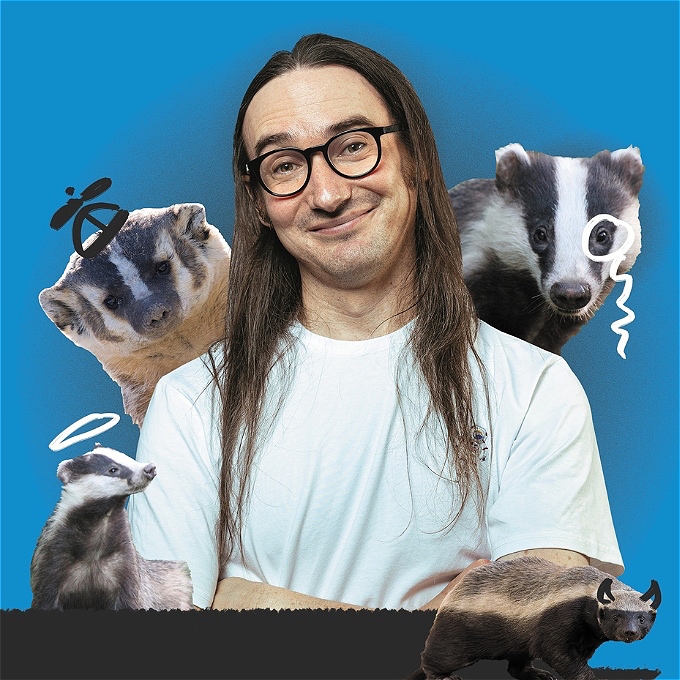 A male comedian smiling surrounded by different types of badgers