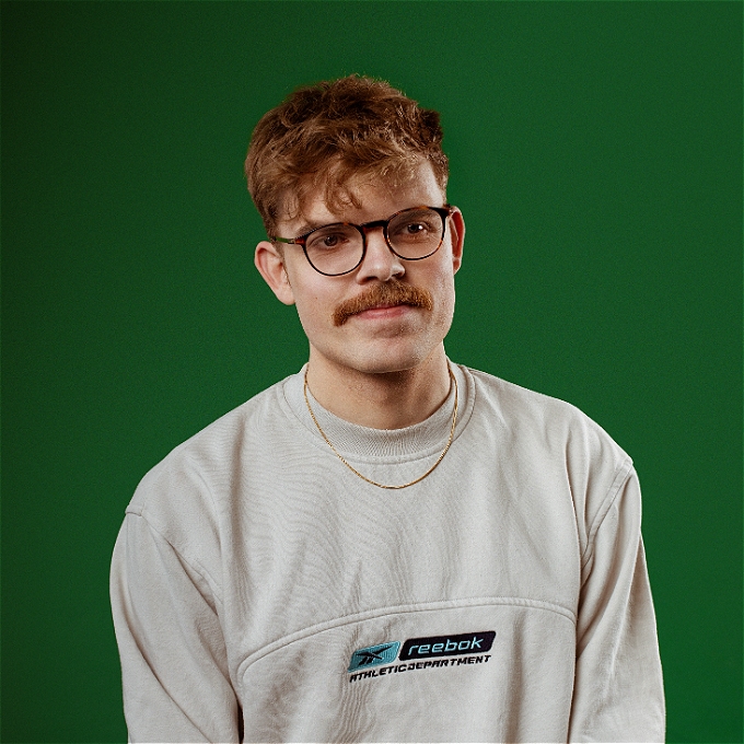 Make comedian with glasses sat down in front of a green backdrop