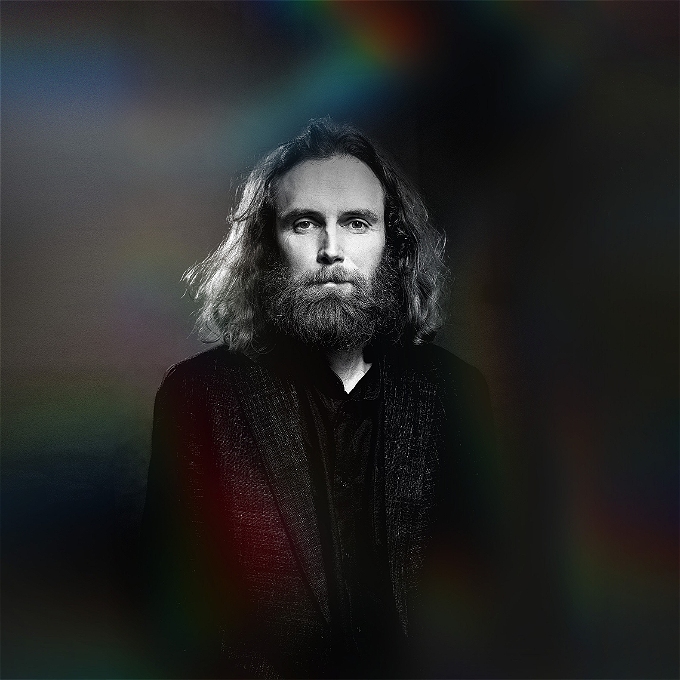 Male comedian with long hair and a busy beard in a grayscale photograph