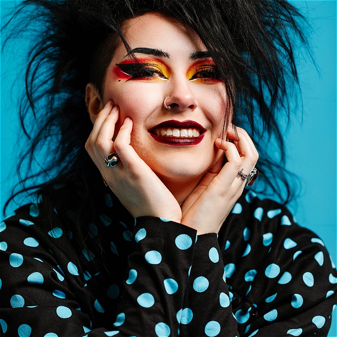 A person with black hair and a black top with blue spots smiling at the camera