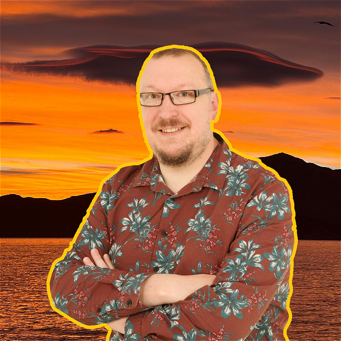 A smiling male comedian with a warm glow standing in front of a sunset on a beach