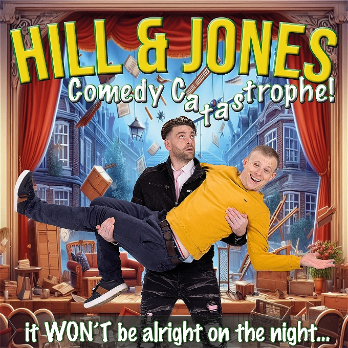 One man standing on a stage, with things falling from the ceiling, carrying another man with a silly expression and his arms outstretched.