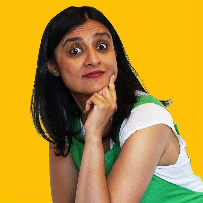 Female comedian with shoulder length black hair in green dungarees on a bright yellow background. She is smiling with curiosity