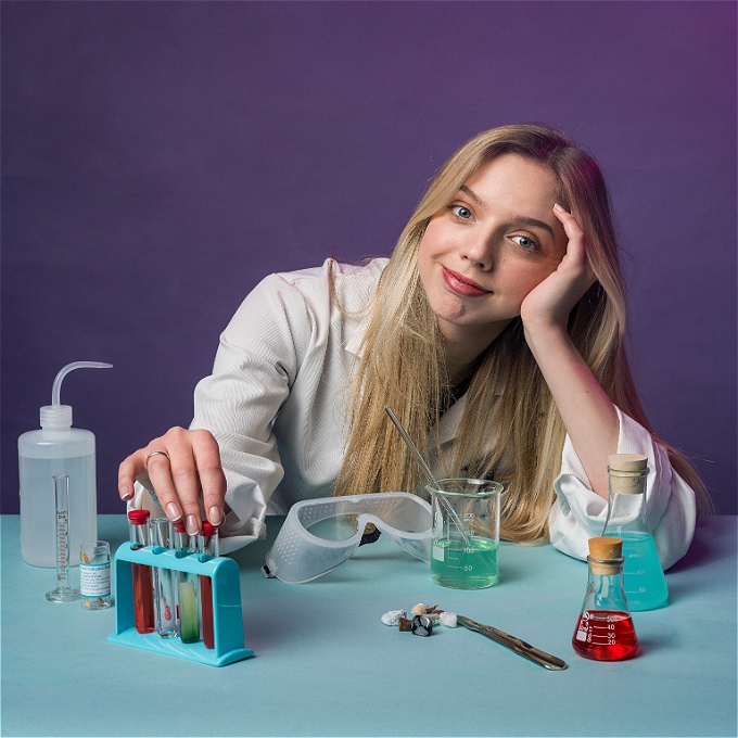 Female comedian with a smile on her face in front of chemistry lab equipment.