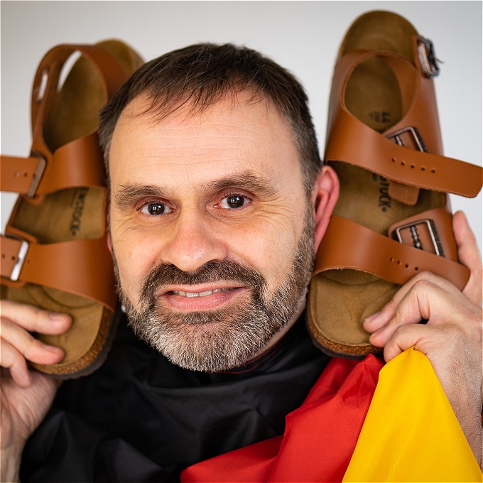 Male comedian with brown hair holding a pair of sandals
