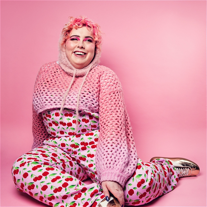A smiling Alison Spittle sits on the floor.