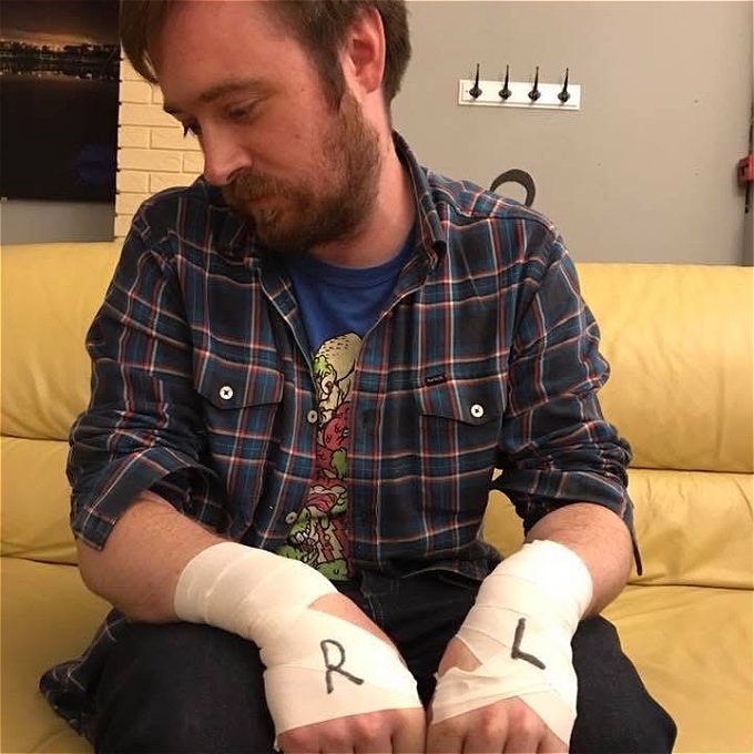 Male comedian with wrist tape on that has ‘R’ & ‘L’ written on it