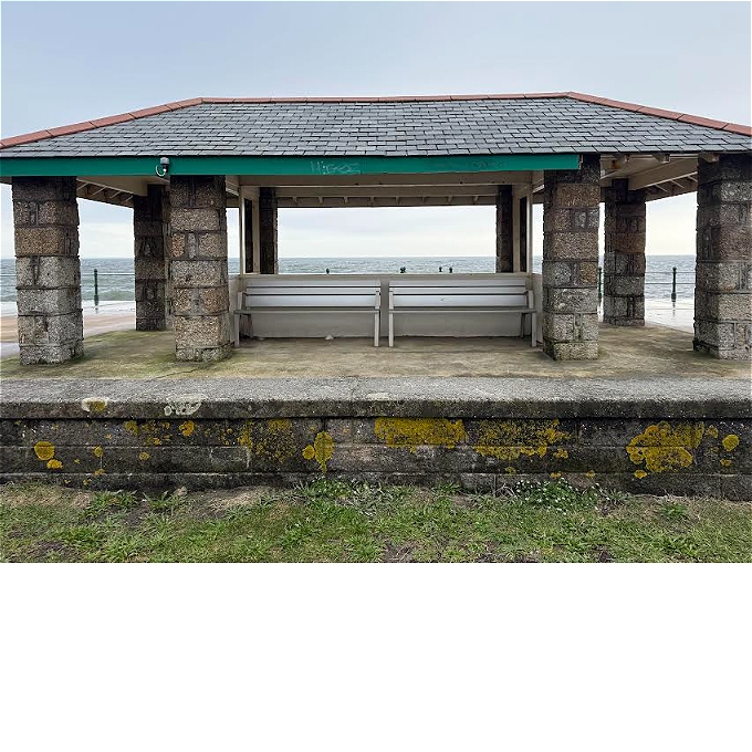 Seafront sheltered seating on the Penzance promenade, benches under roof looking out to sea