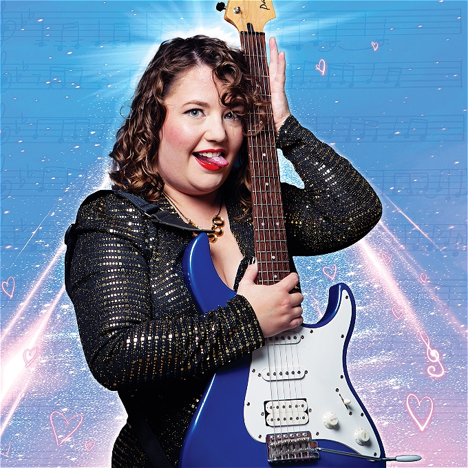 Female comedian with brown curly hair clutching her electric blue guitar to her chest while smiling and poking her tongue towards the guitar as if she's going to lick it. With a blue and light pink background.