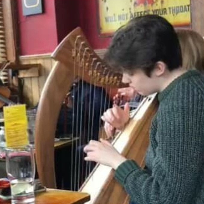 Female comedian with short brown hair and a green jumper plays a small harp in a pub.