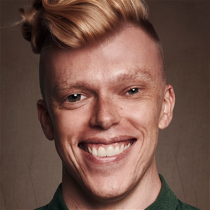 An altered image of a broadly smiling Jordan Brookes with an extravagant quiff, severe undercut and slightly too large left eye.