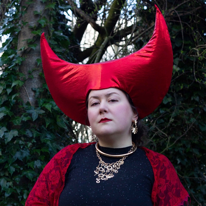 Jain Edwards looks sternly at the camera while wearing a bright red hat that peaks to two high points.