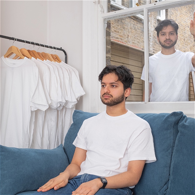 Rohan Sharma sits on a sofa, staring off screen. Behind him is a mirror, into which a second Rohan Sharma looks in, directly at the camera.