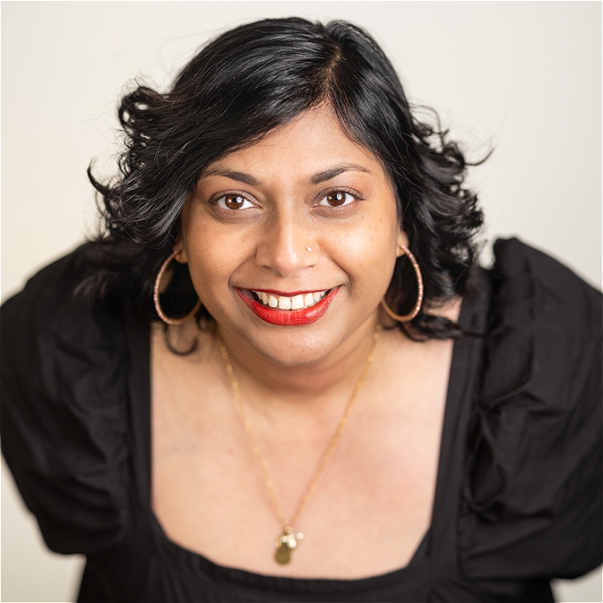 Female comedian with dark brown hair big smile with red lipstick big eyes big hoop earrings and black dress
