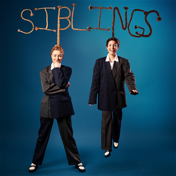 2 female comedians (sisters) hanging by their hair off the word Siblings, which is made out of their hair