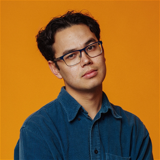 Comedian with glasses and blue shirt looks at camera