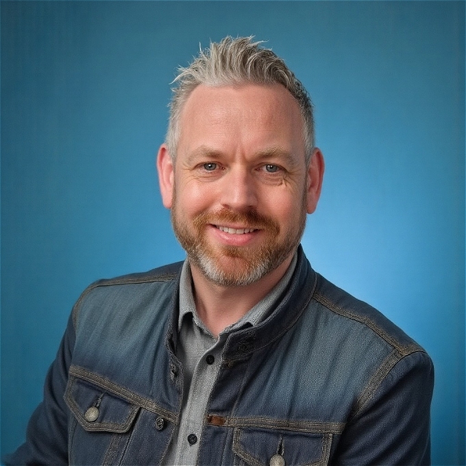 Comedian Mark Row in a denim jacket with a glint in his eye that shows that he's dreaming of a life beyond the classroom
