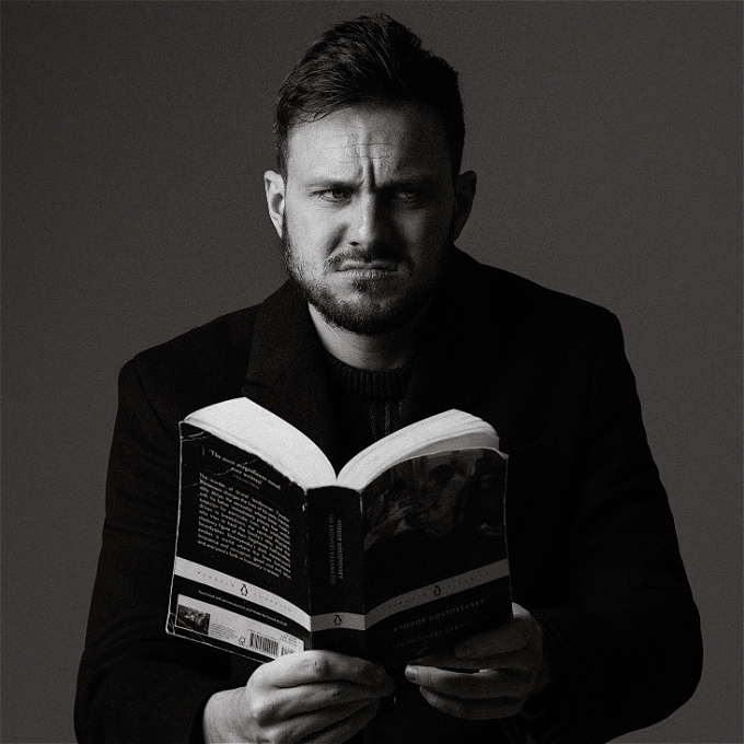 Male comedian sits with an open book and a dissatisfied expression