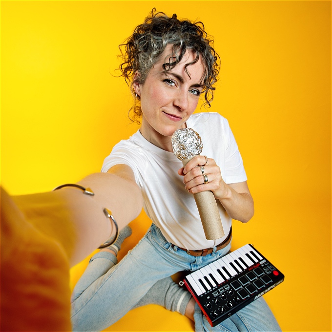 Female comedian with curly hair holding a toy microphone and a small piano
