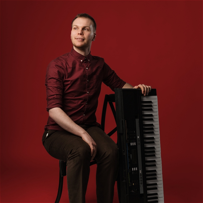Male comedian sitting at a chair, holding a keyboard like a proud father