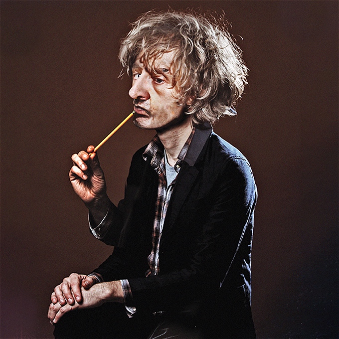 A composite of several images of Richard creating one with three eyes and three arms posing quite naturally, two hands on lap, one sucking a pencil.