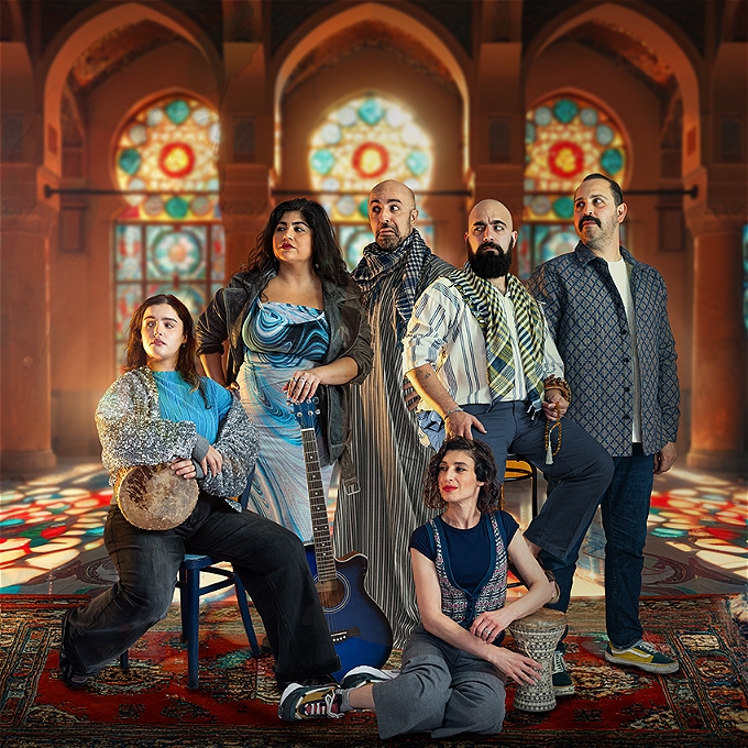 Six performers with instruments sitting in front of a stained glass window react to something bizarre occuring out of frame.