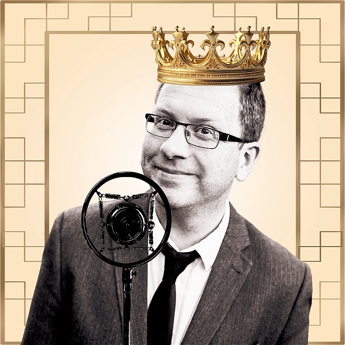 Black and white picture of Paul Kerensa, wearing a crown, in front of an old-fashioned radio mic