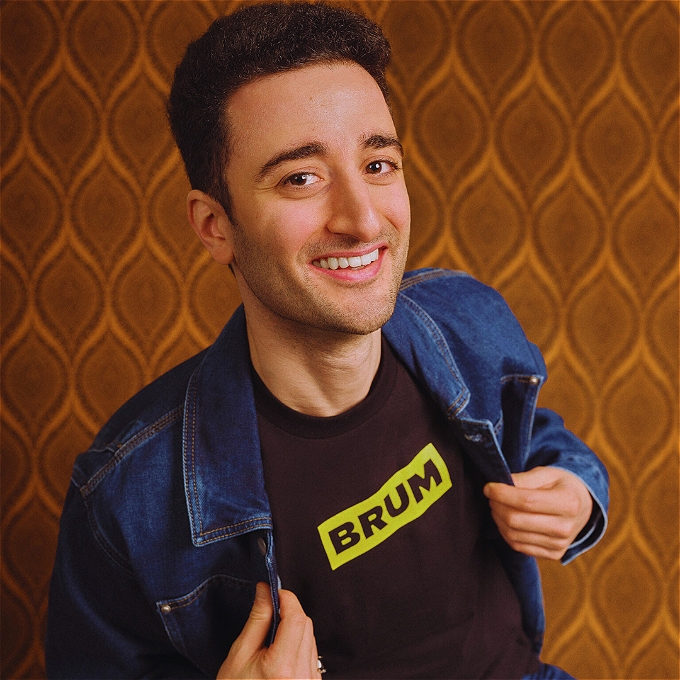 Comedian Hasan Al-Habib holding a denim jacket open to reveal the word 