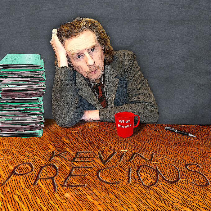 Male comedian sitting at a teacher's desk looking exhausted