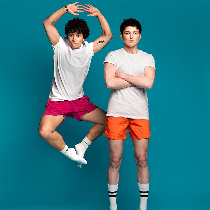 two comedians. one standing arms folded and one jumping in the air