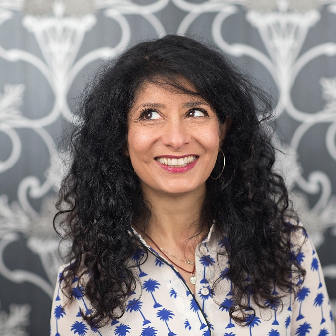 Female comedian of colour with dark hair in front of a grey background