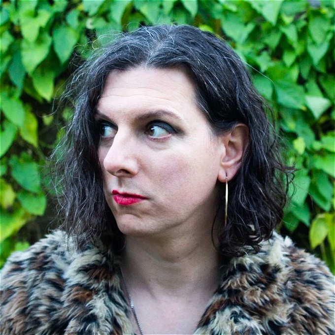 Nonbinary comedy in front of deep green bush