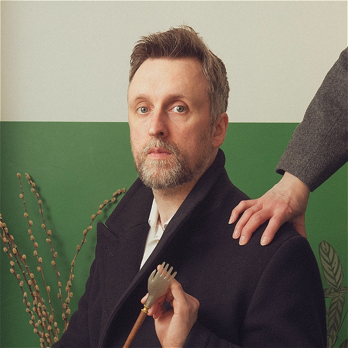 A solemn Matt Winning holds a small hand pointer, another, human, hand rests on his shoulder