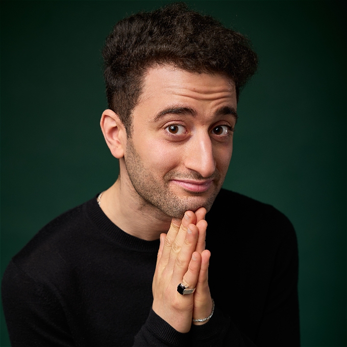 Comedian Hasan Al-Habib with his hands clasped as if they were in prayer, smiling