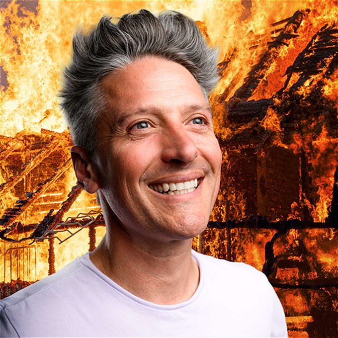 Stuart Goldsmith smiles broadly against a background of burning building