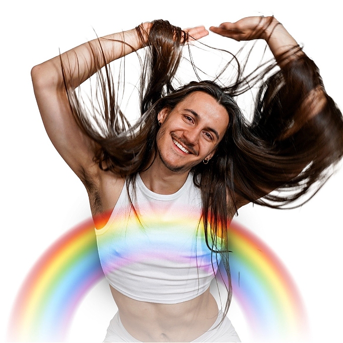 Genderfluid musical comedian with long brown hair smiles and throws their arms up in front of a rainbow with a white background