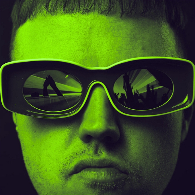 Close up of Adam Flood wearing oversized sunglasses the reflections on which depict hands held high at a rave
